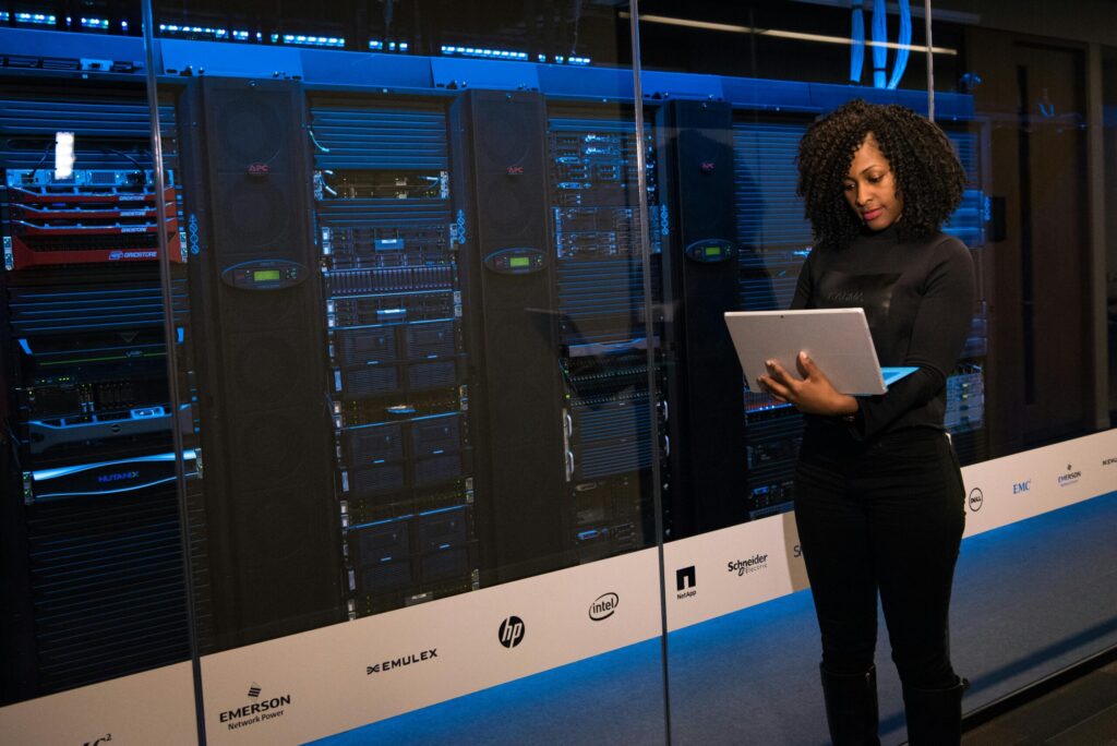 A female engineer using a laptop while monitoring data servers in a modern server room, representing the different aspects of the cybersecurity principle, CIA Triad