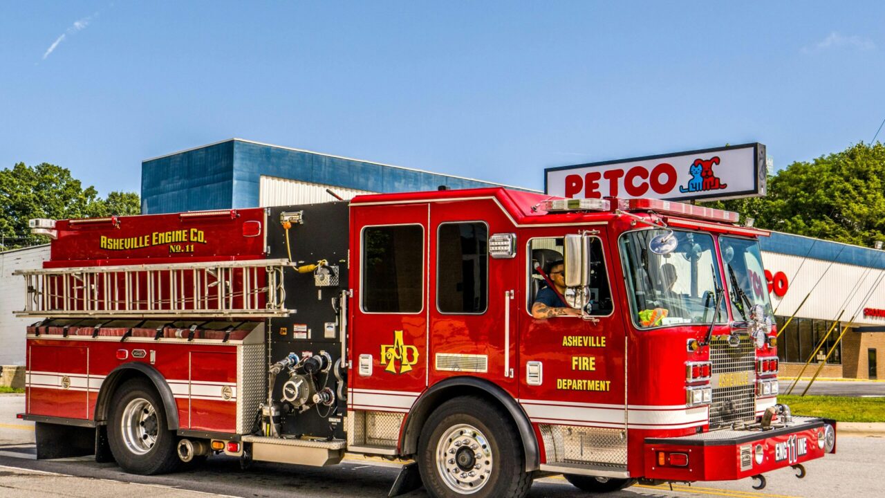 Vibrant red fire truck from Asheville Fire Department parked outside Petco on a sunny day.