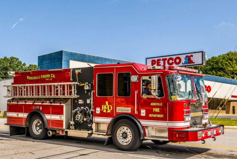 Vibrant red fire truck from Asheville Fire Department parked outside Petco on a sunny day.